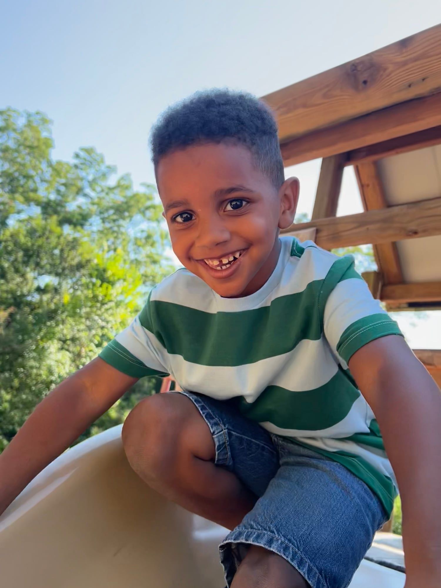 A boy smiling at the top of a playground slide
